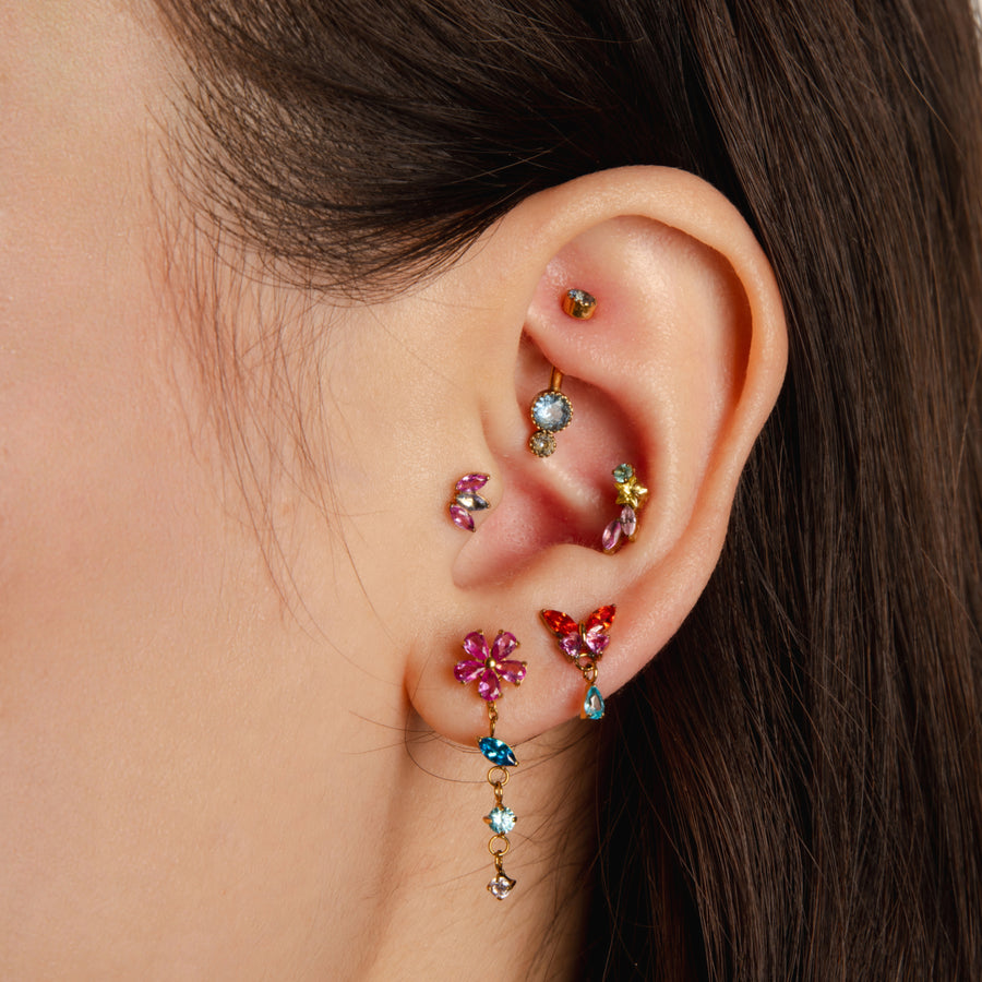 Close-up of an ear with colorful gemstone earrings on a neutral background