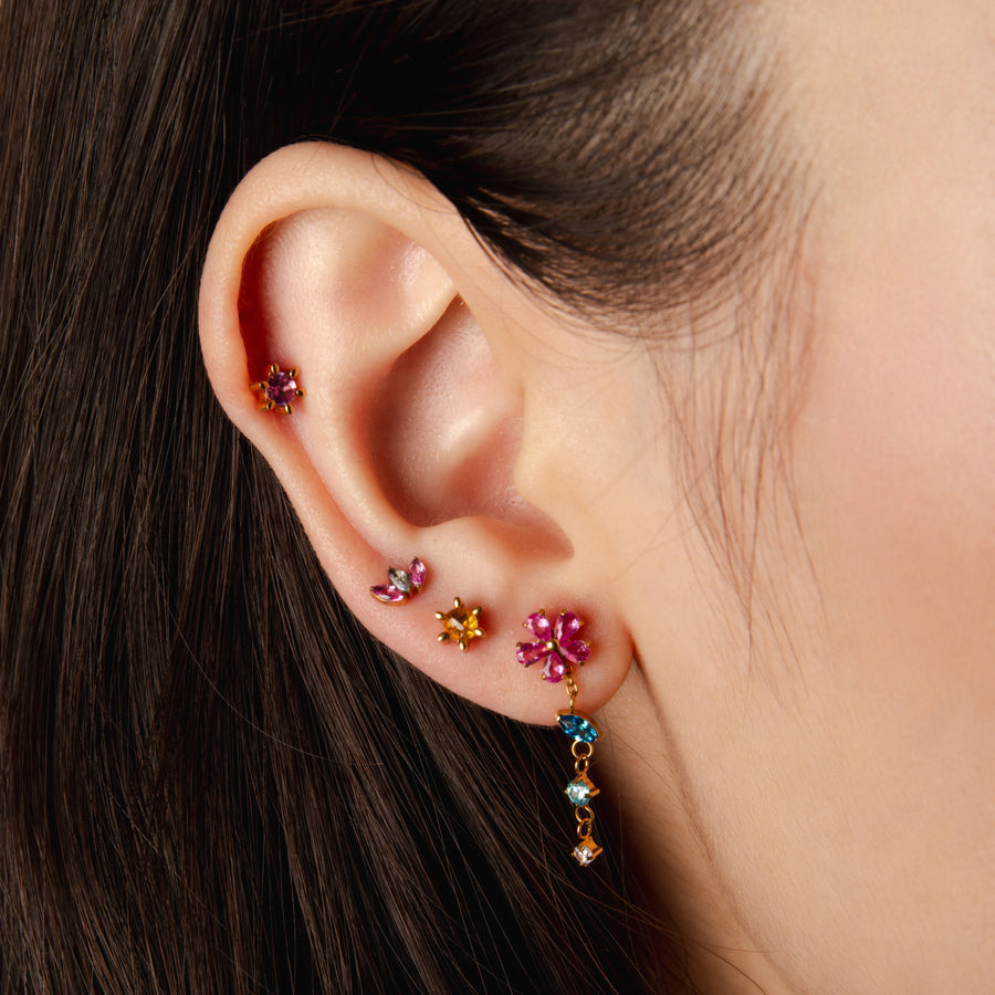 Close-up of an ear with colorful gemstone earrings on a neutral background
