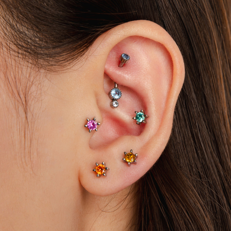 Close-up of an ear with colorful gemstone earrings on a neutral background