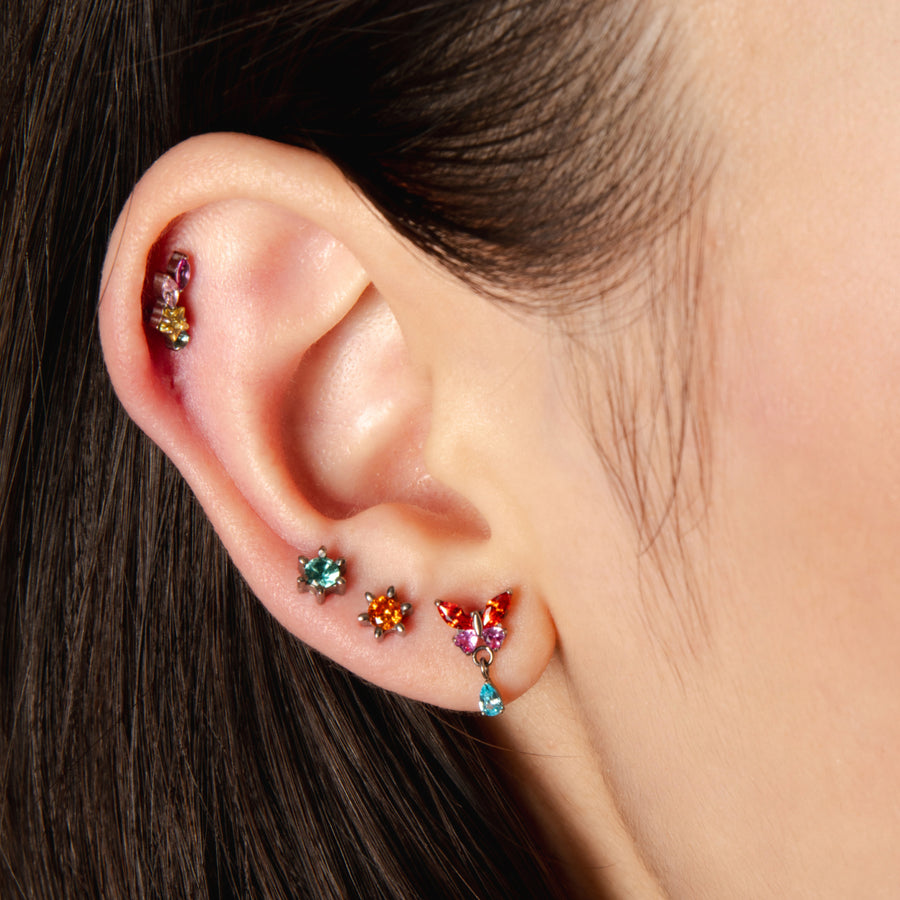 Close-up of an ear with colorful gemstone earrings on a neutral background