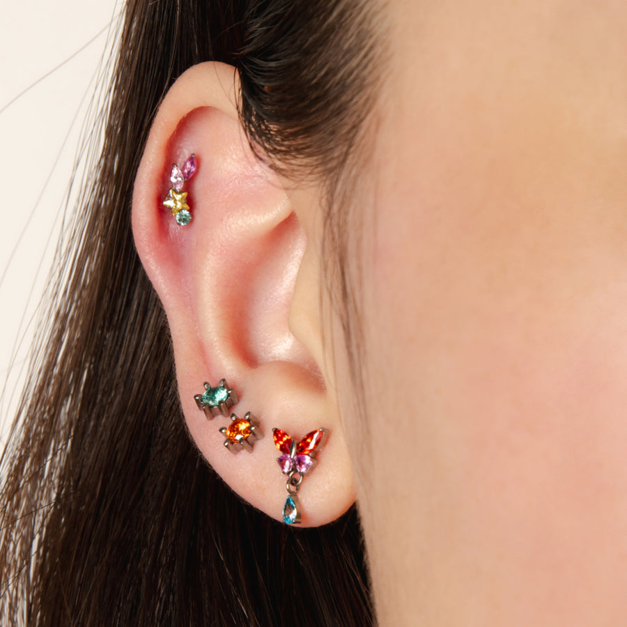 Close-up of an ear with colorful gemstone earrings on a neutral background