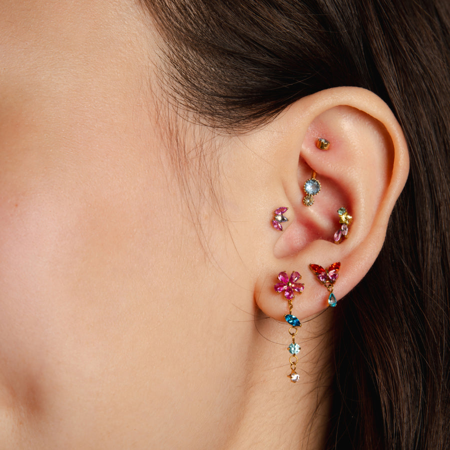 Close-up of an ear with colorful gemstone earrings on a neutral background