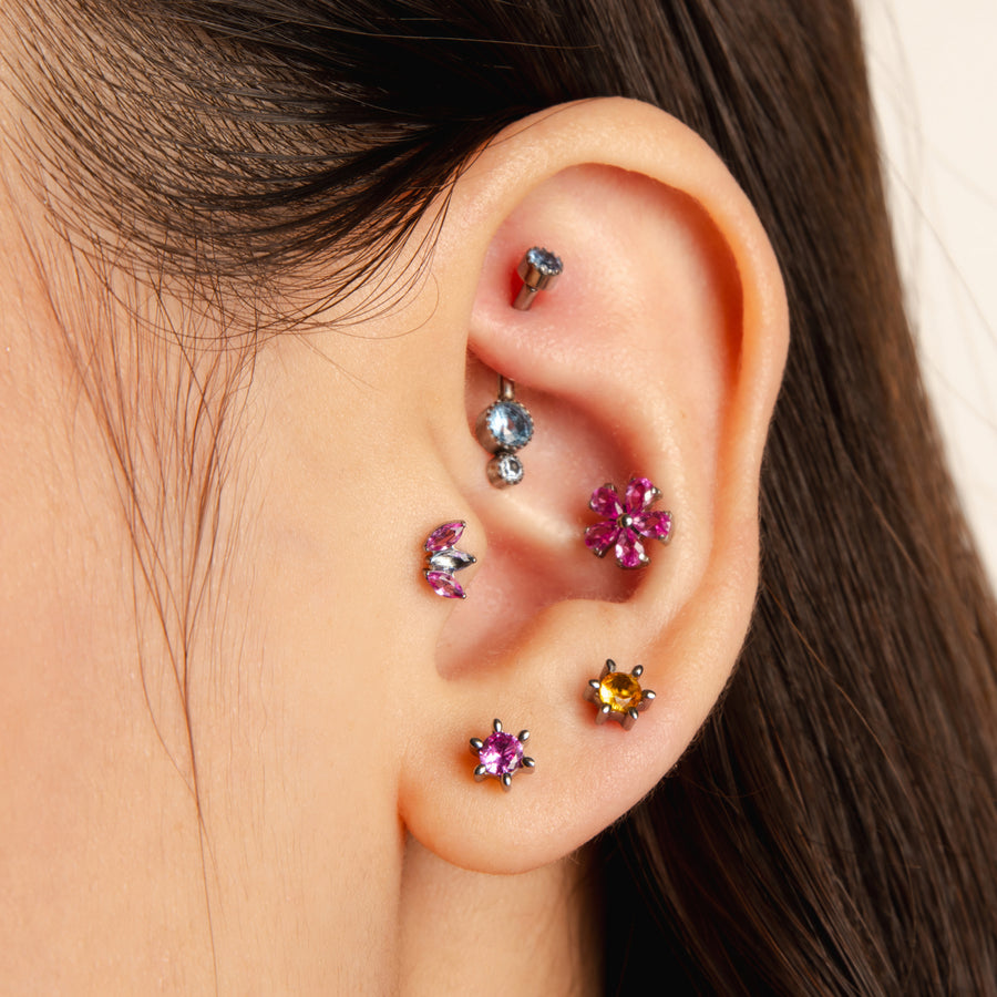Close-up of an ear with colorful gemstone earrings on a neutral background