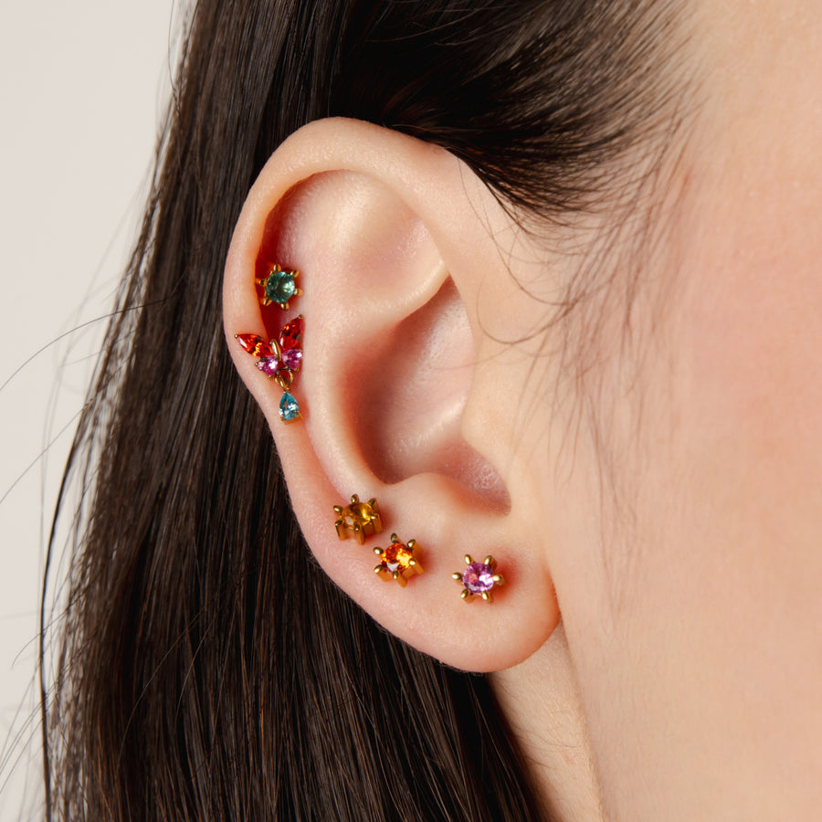 Close-up of an ear with colorful gemstone earrings on a neutral background