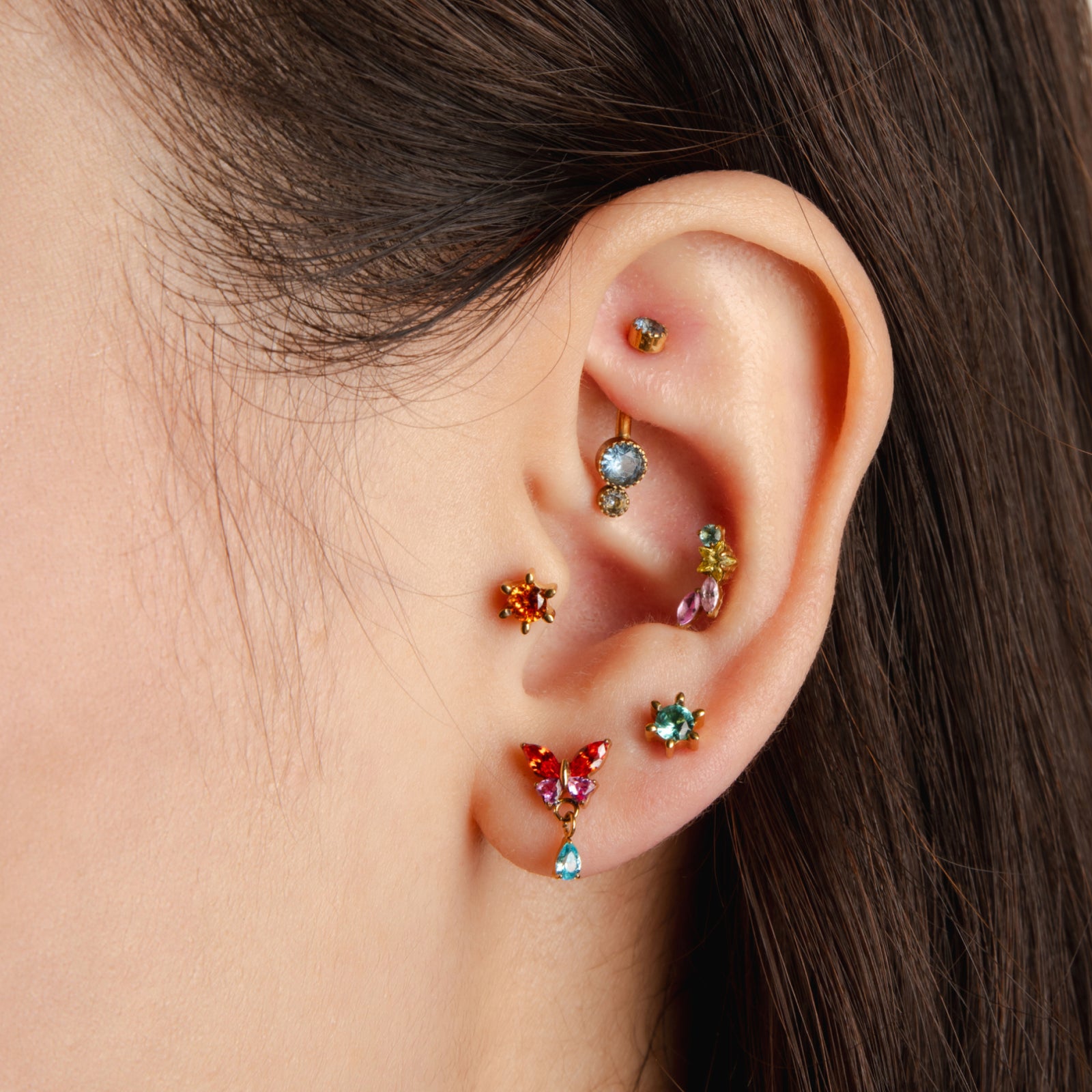 Close-up of an ear with colorful gemstone earrings on a neutral background