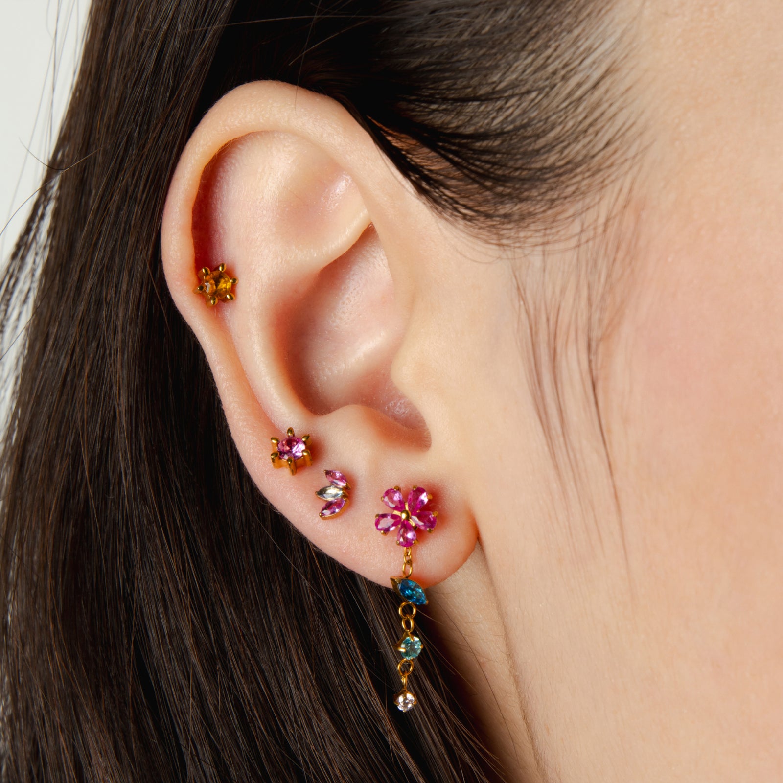 Close-up of an ear with colorful gemstone earrings on a neutral background