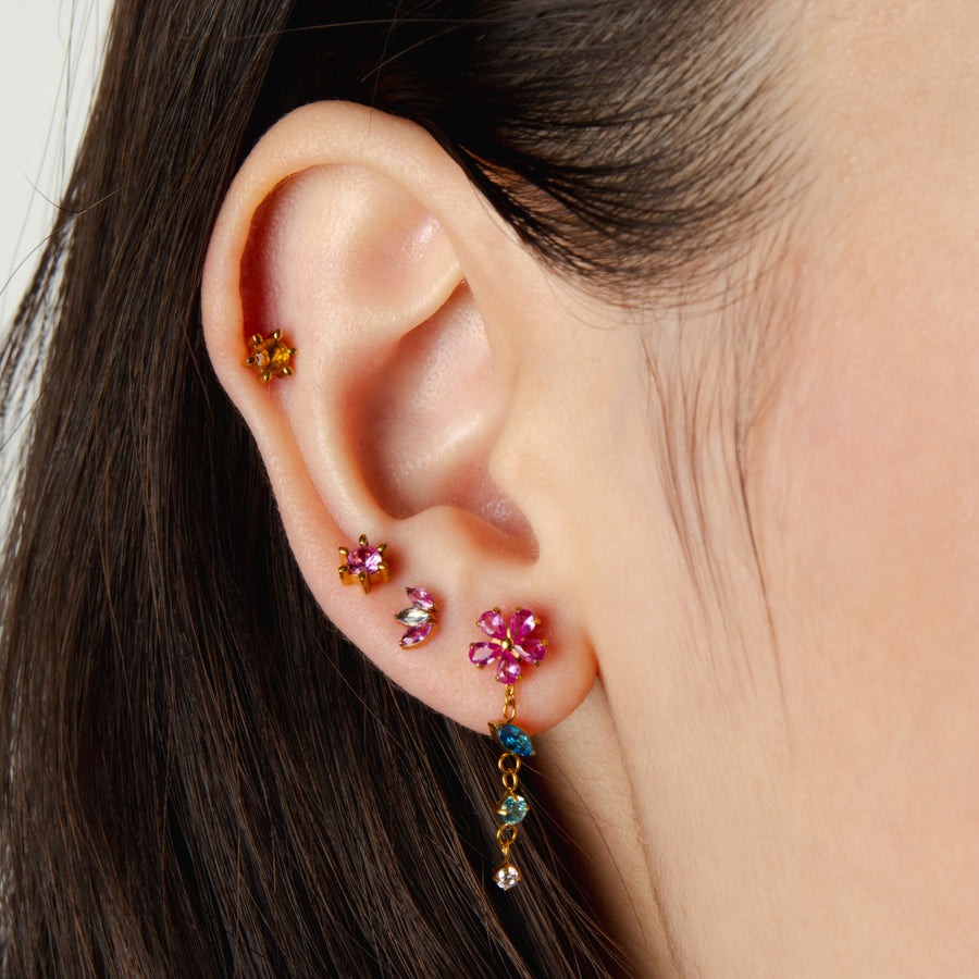 Close-up of an ear with colorful gemstone earrings on a neutral background