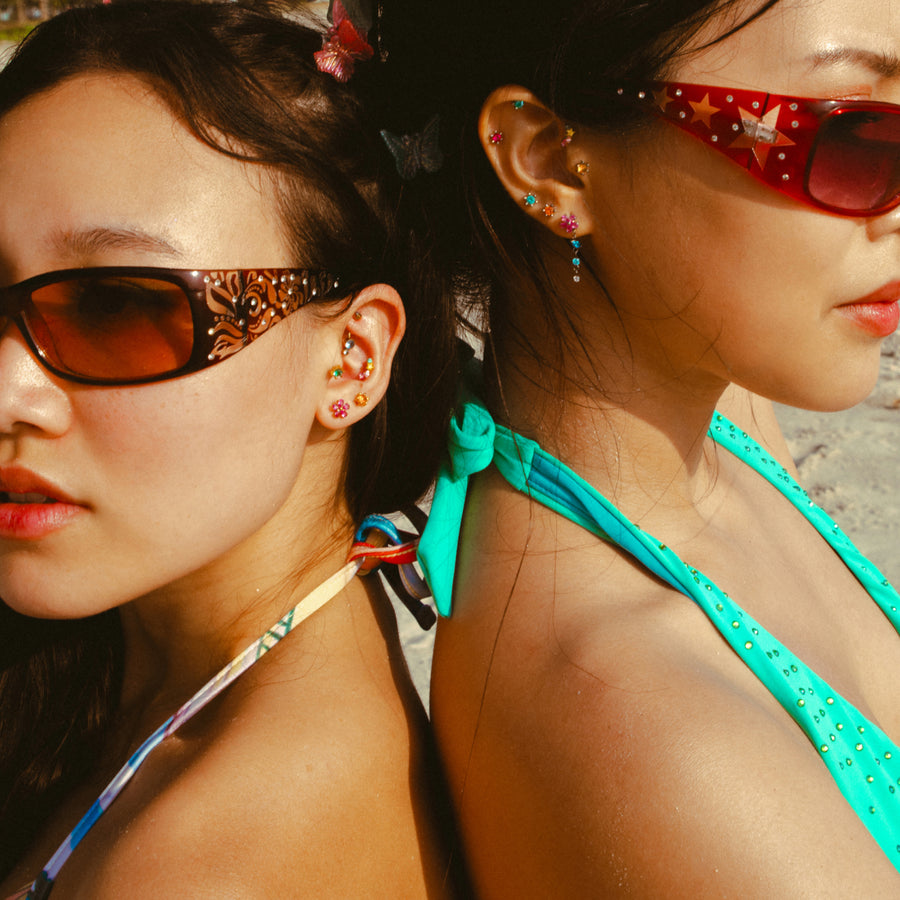 Two women wearing sunglasses and colorful earrings on a beach.