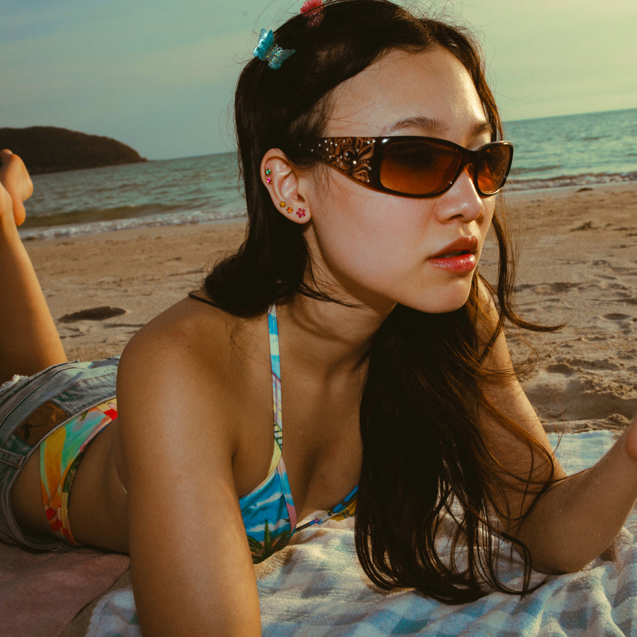 Woman wearing sunglasses and a colorful bikini and earrings on a beach